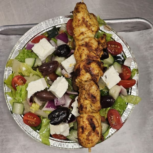 Grilled chicken skewer over a fresh Mediterranean salad with feta, olives, tomatoes, and cucumbers.