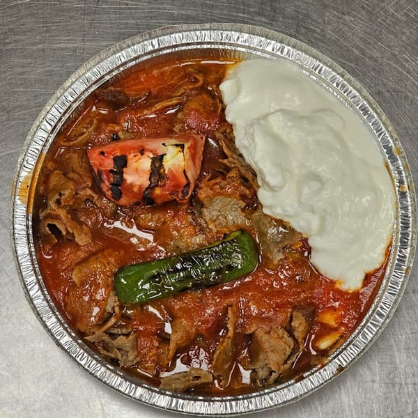 Iskender kebab with tomato sauce, grilled tomato, pepper, and yogurt in a foil container.