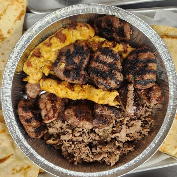 A Kapadokia Grill platter with grilled meatballs, chicken, and shredded meat in a foil container.